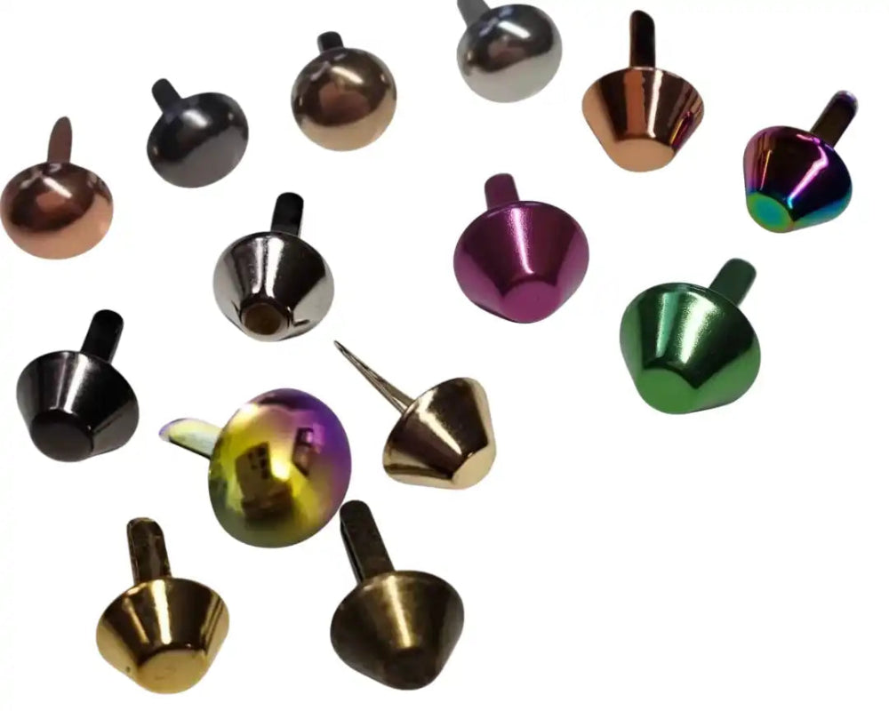 Eine Sammlung von Metallnieten und Rivets in verschiedenen Formen, Größen und metallischen Oberflächen, einschließlich runder, konischer und facettierter Designs, wobei einige eine spitze Zunge zur Befestigung aufweisen.